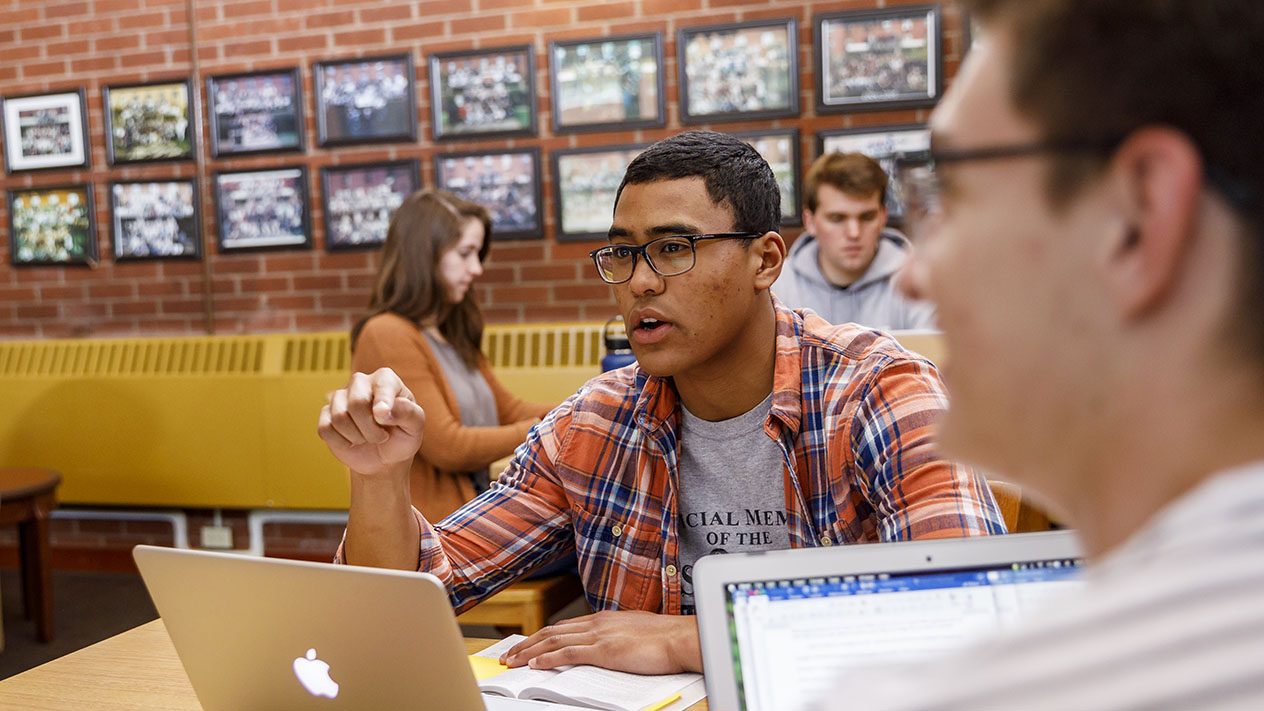 A young student shows enthusiasm while discussing a class project with their group at a table