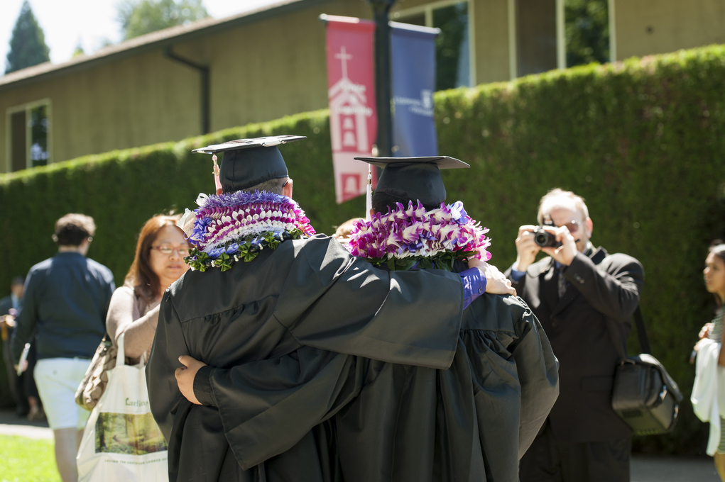 Two men in graduation gowns embrace each other joyfully, celebrating their achievement together.