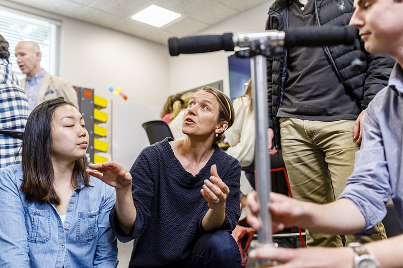 A group is gathered, kneeling, while examining a project in a classroom