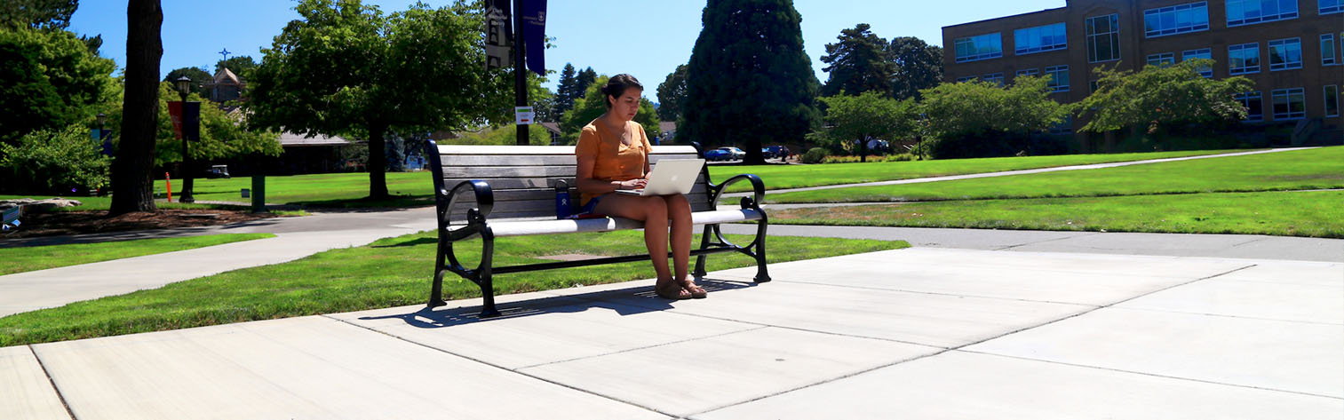student with a laptop sitting on a bench outdoors
