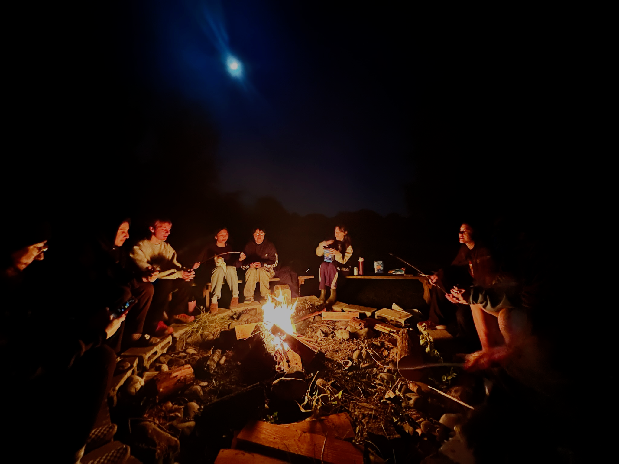 Students sit around a campfire and reflect on the day while toasting marshmallows