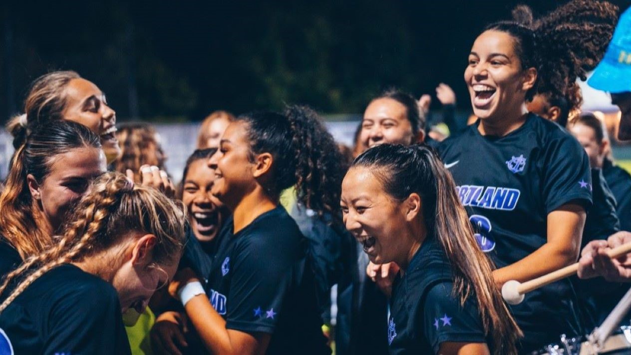 Women's soccer team players celebrate on the field post game.