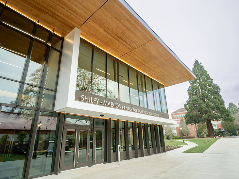 An exterior view of the Shiley Marcos Center, a large modern flat roof building with a wall of windows, at sunset.