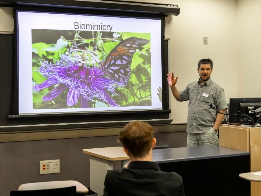 A professor stands in front of a projection screen with an example of an AI generated image