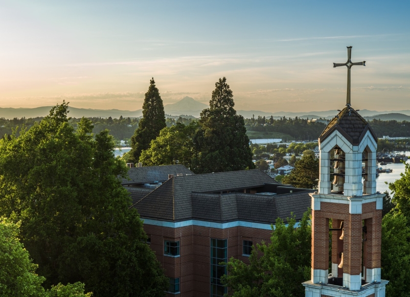 A mid-air drone image of the bell tower with the sun rising over the mountains in the background