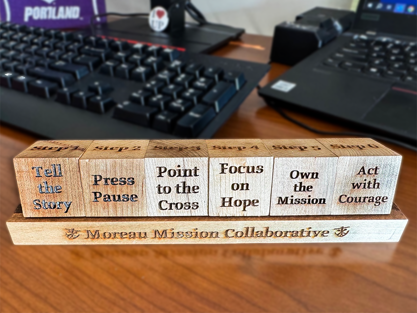 line of wooden blocks with inspirational actions burned into them, on top of a base block that says 'Moreau Mission Collaborative'