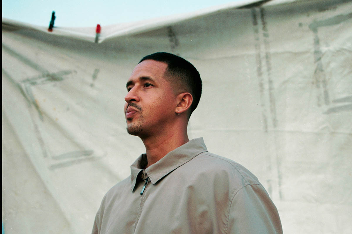 Alum Walter Thompson-Hernandez standing side profile in front of a cloth backdrop and dusk sky.