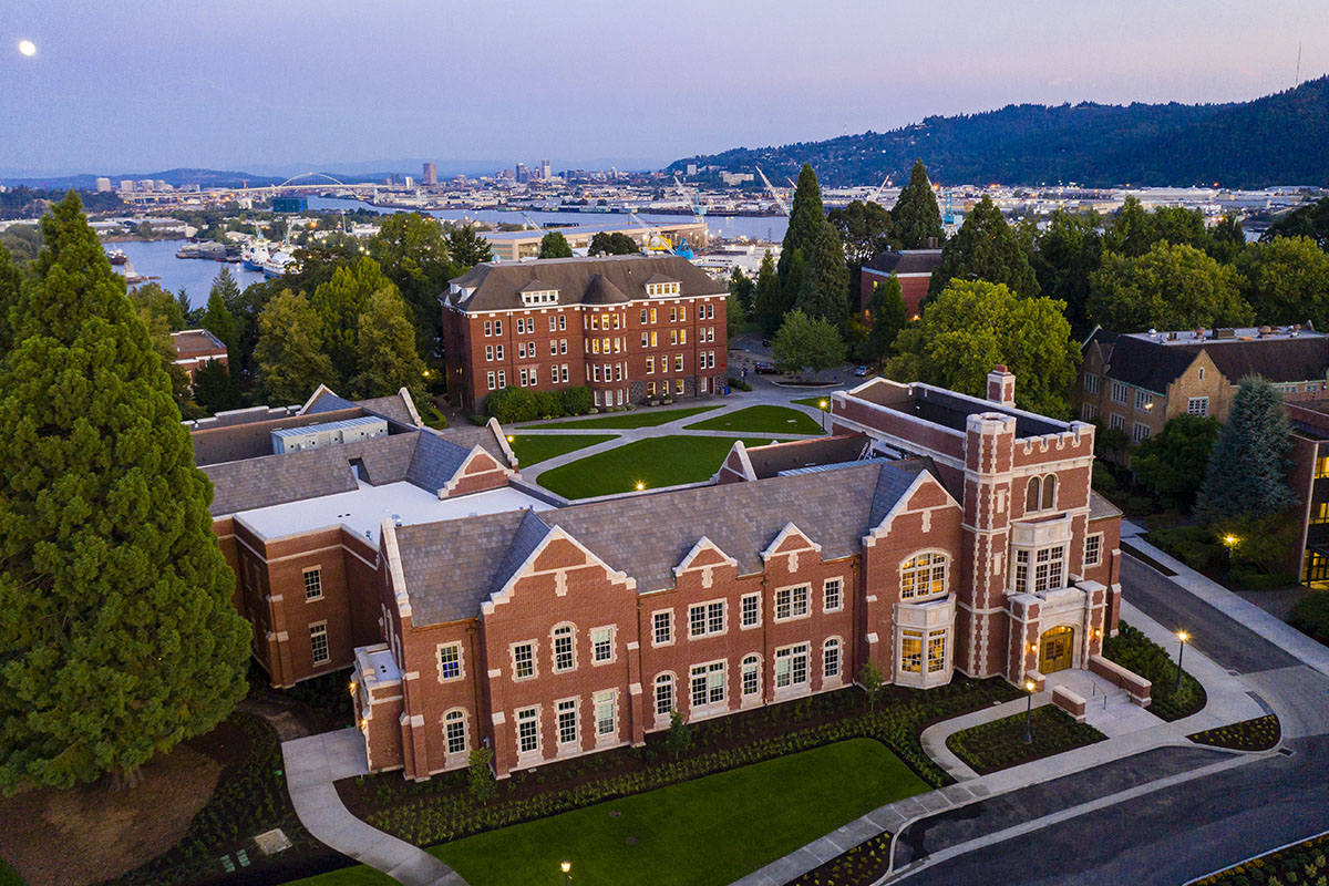 Aerial view of Dundon-Berchtold Hall at dusk with downtown Portland, the river, and a full moon rising in the background.