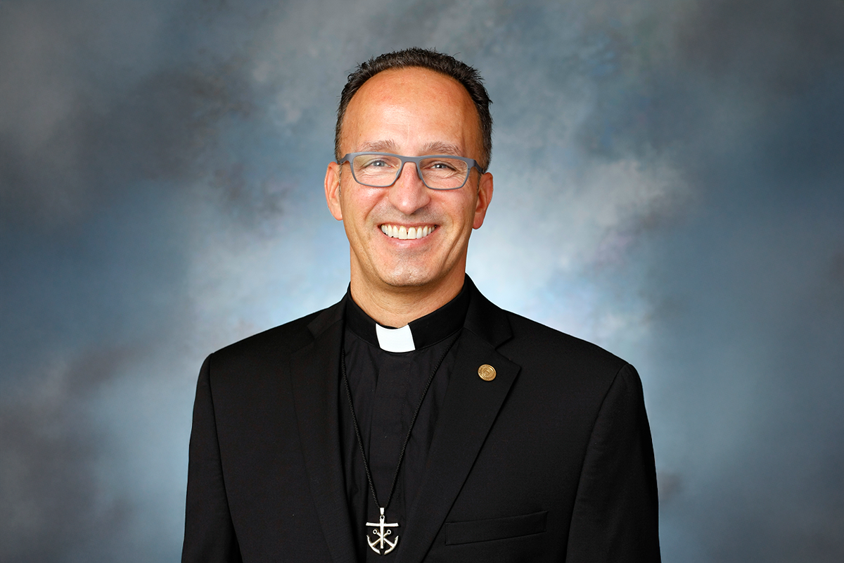Father John Donato against a blue portrait backdrop, smiling.