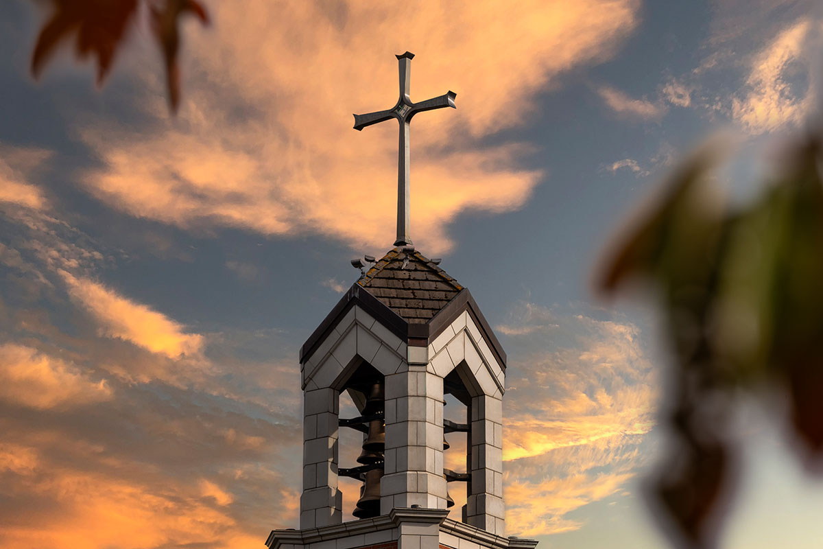 Bell Tower Cross against a beautiful sunset sky with pink and orange clouds.