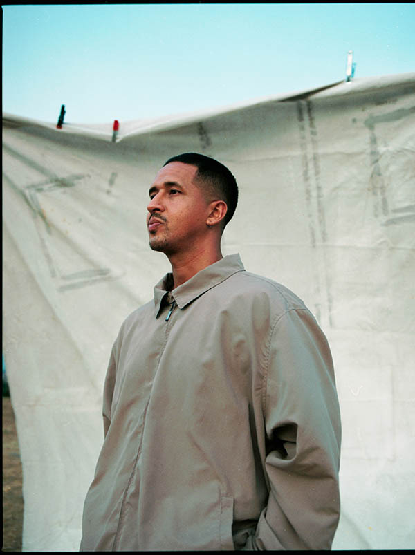 Alum Walter Thompson-Hernandez standing side profile in front of a cloth backdrop and dusk sky.