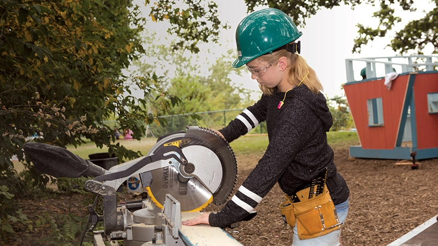 A girl with a hard hat uses a chop saw