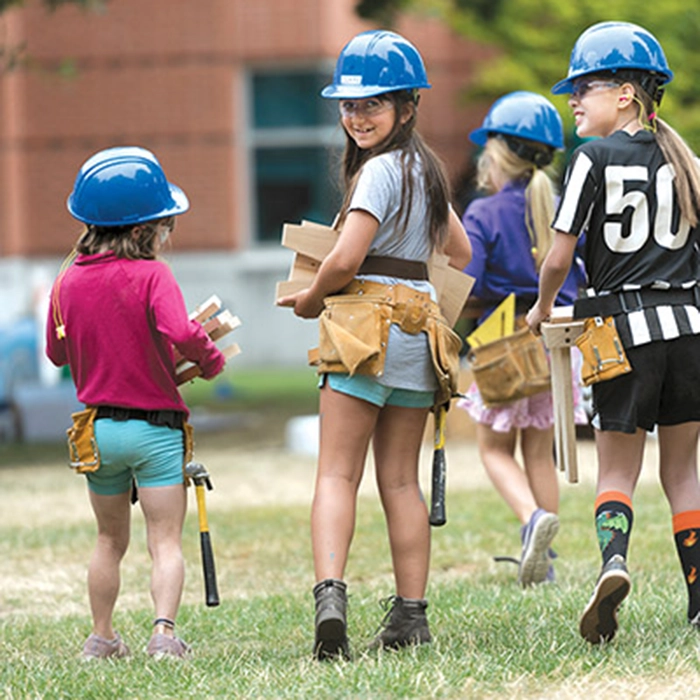 A group of young girls with hard hats on walking with construction materials