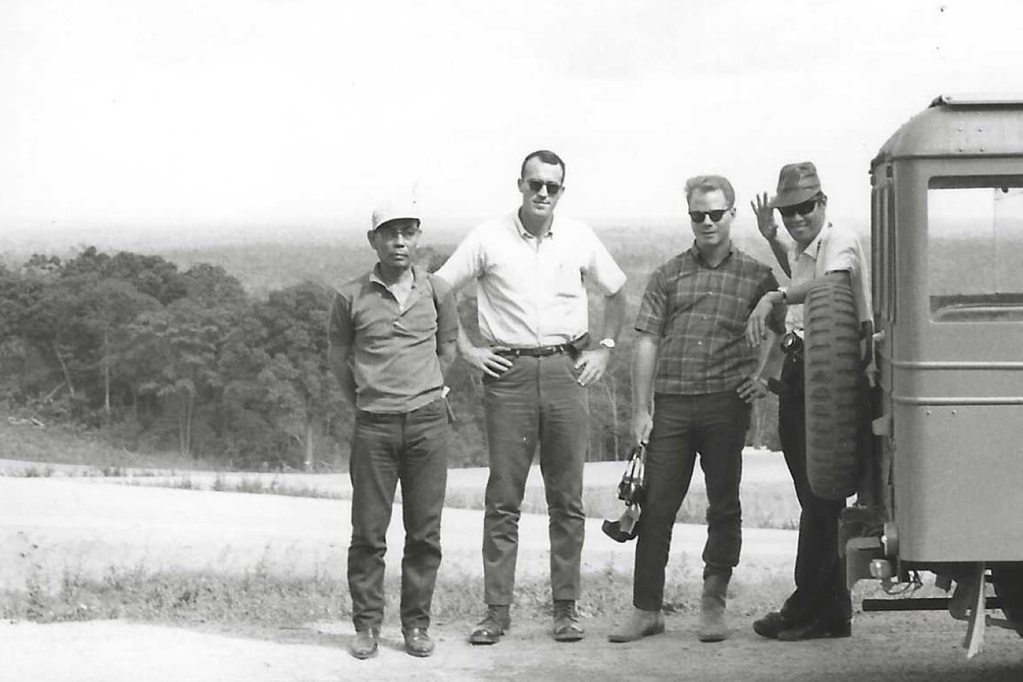 A black and white photograph from the 1960's of Mike Burton (second from left) in a Laotian village, accompanied by a member of the US embassy and translators.