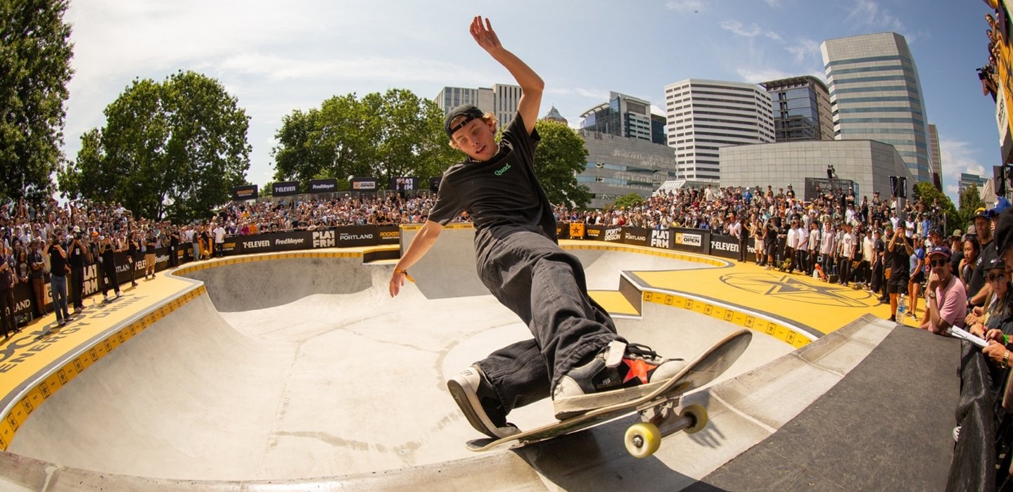 A fisheye style image of a skateboarder in a half pipe surrounded by a cheering crowd in downtown Portland