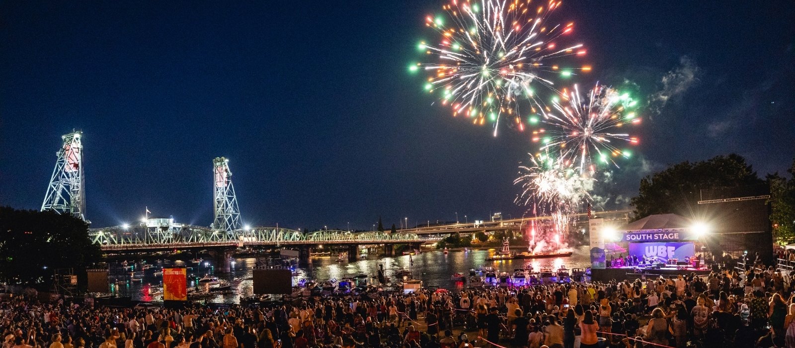a large crowd of people watching fireworks over the river in downtown Portland