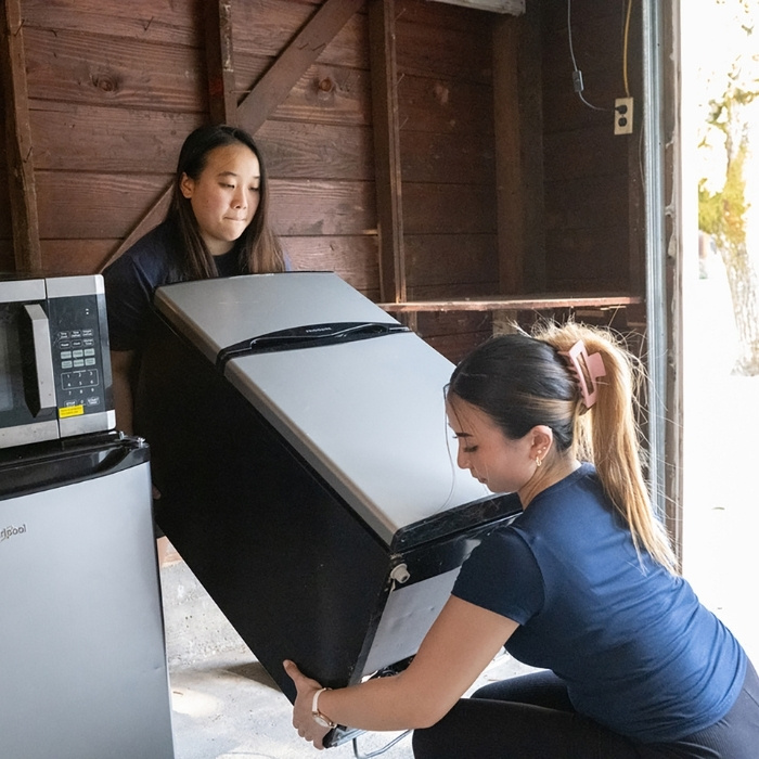 Two students move a mini refrigerator into a storage unit