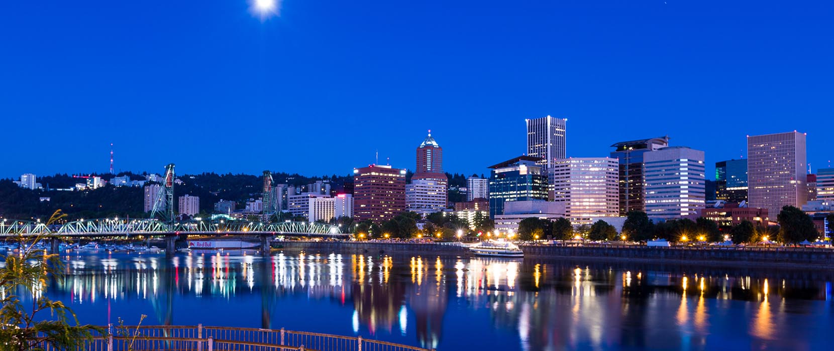 A nighttime view of downtown Portland with lights reflecting off of the surface of the river