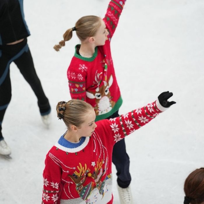 Two figure skaters wearing holiday sweaters pose on the ice for a performance.