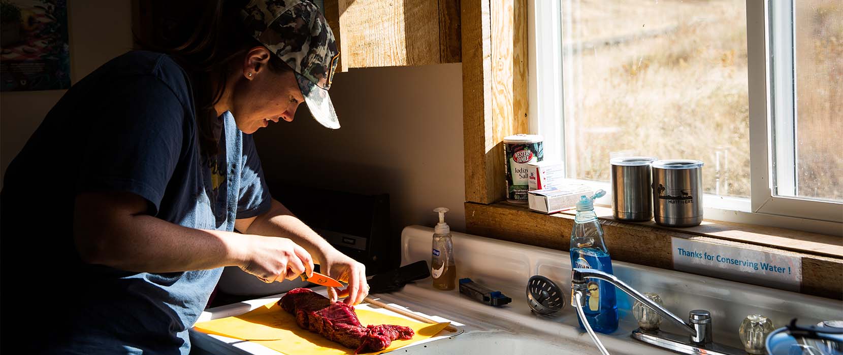 Chelsea Cassons, in her hunting cap, cuts meat in her kitchen