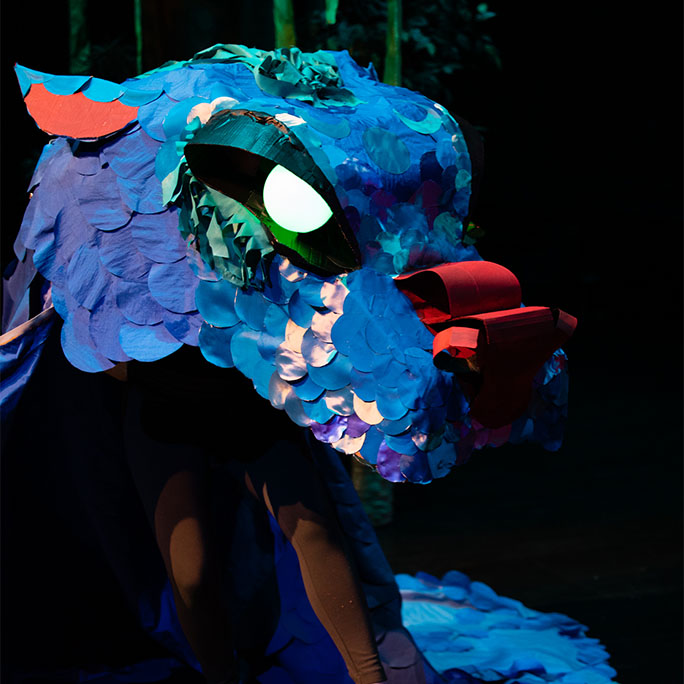 a dragon puppet made from blue and green fabric with LED eyes and a red cardboard nose