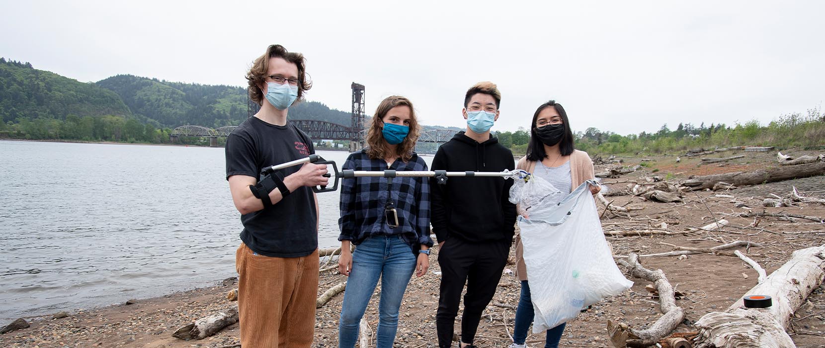 students hold a litter grabber and a bag of trash along the riverfront