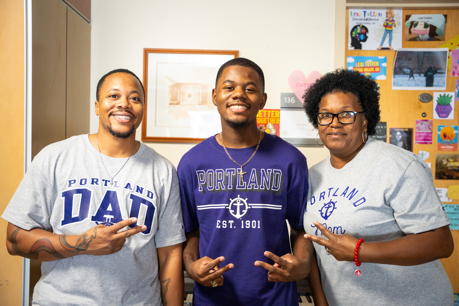 Photo of family (left to right mom, son, dad) posing during Move In in their University of Portland shirts.