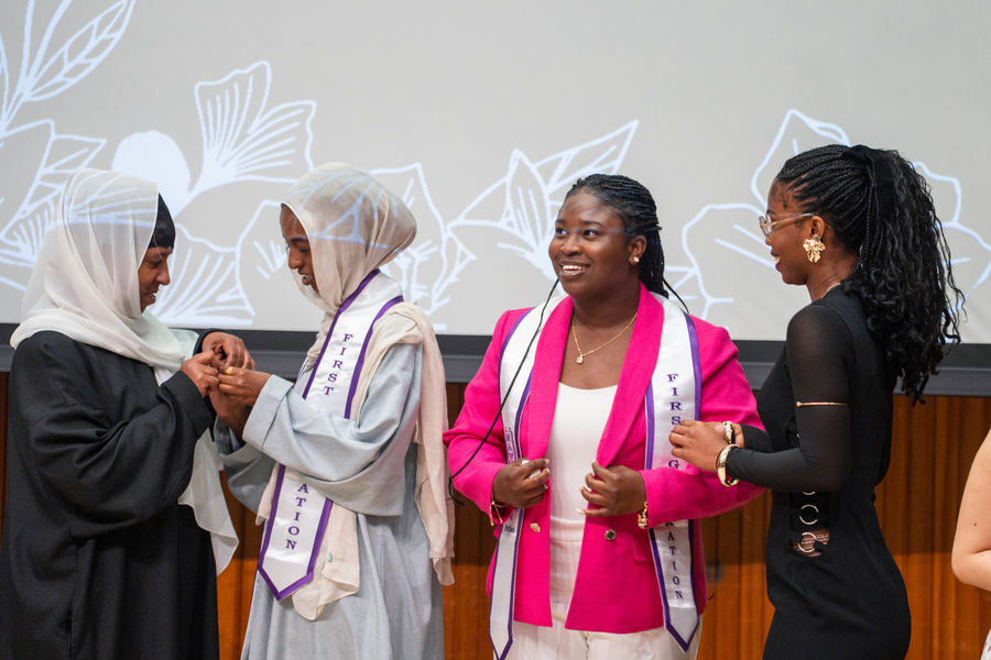 Photo of several First Generation students at their pinning ceremony. Two of them are turned toward each other, placing a pin, while the other two look out and smile.