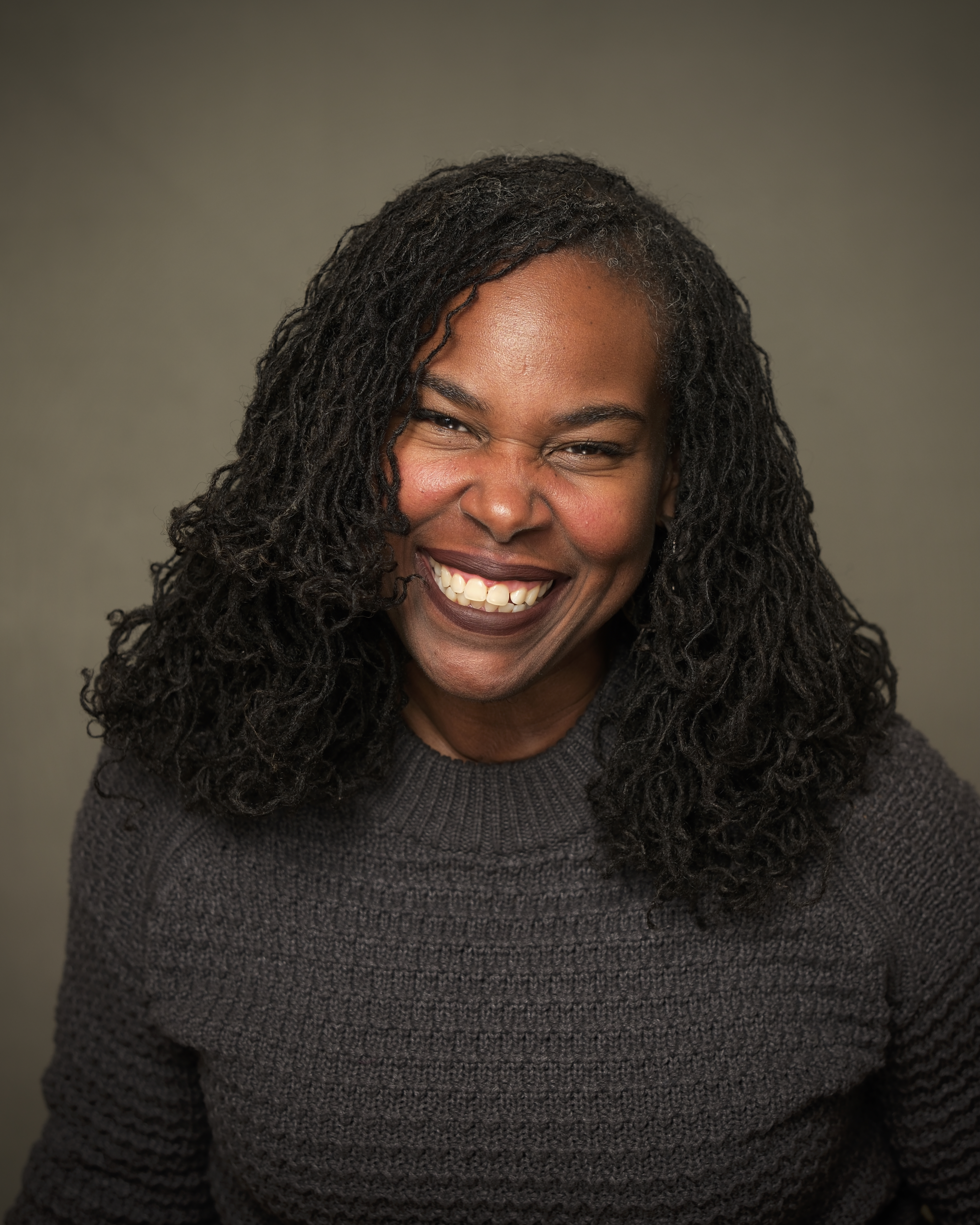 Renée Watson, a black woman with long dark hair and a grey shirt smiles toward the camera