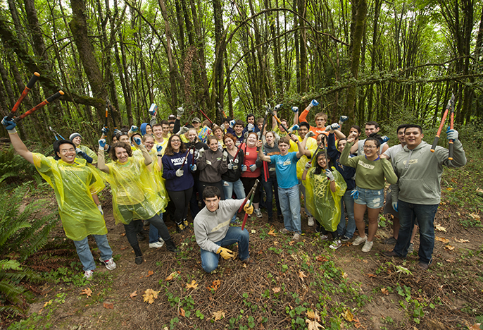 Dozens of students in the forest with arms and clippers raised