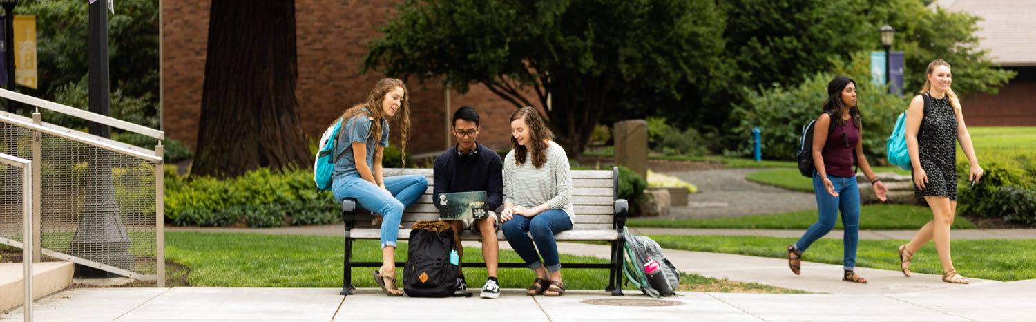 Students sit on a bench outdoors.